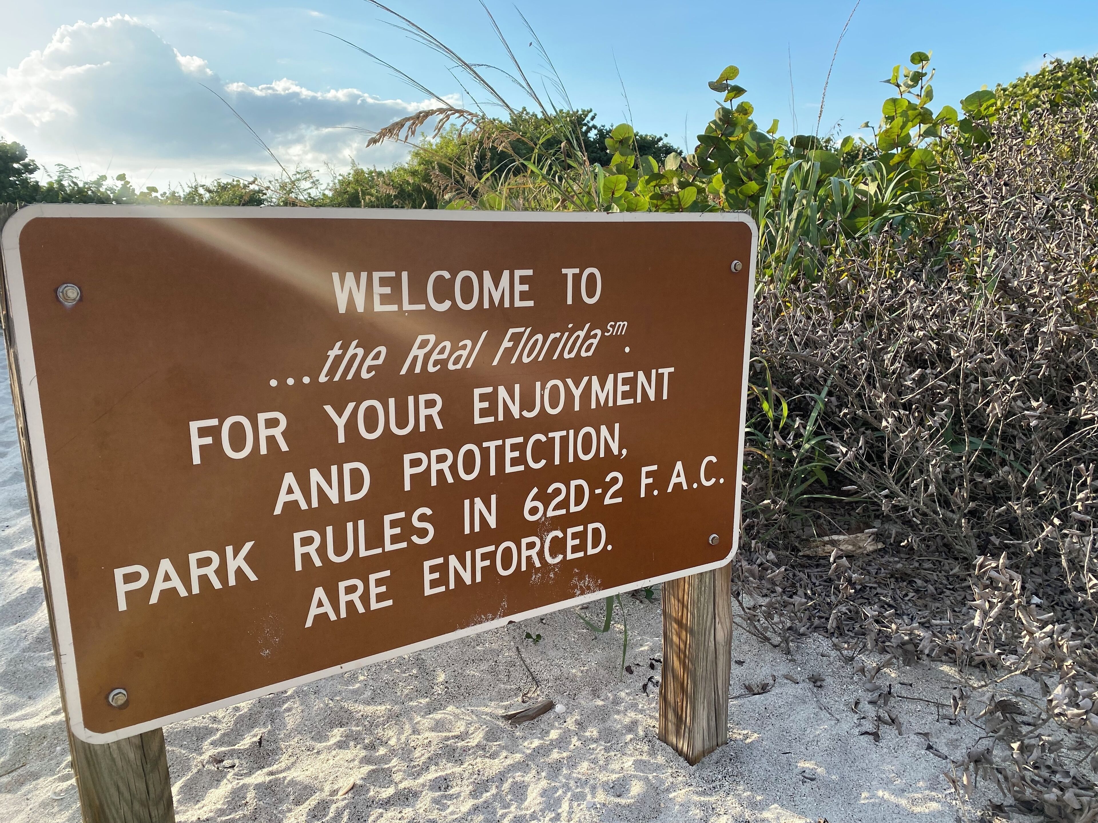 Braunes Schild mit weißer Schrift, das Besucher im Real Florida Park willkommen heißt und Parkregeln erwähnt.