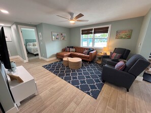 A living room with a sectional sofa, a gray armchair, a coffee table, and a ceiling fan. - COCO BUNGALOW - All new w/ heated pool, bikes, beach equipment & more (Englewood)