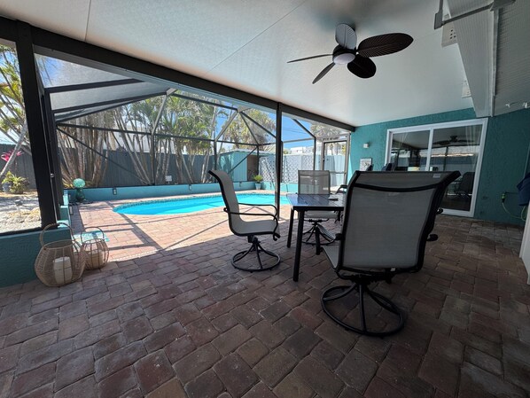 Eine überdachte Terrasse mit Pool, Sitzgelegenheit im Freien und Deckenventilator.