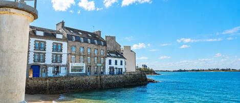 A coastal building with multiple windows and balconies, situated near a clear blue sea.