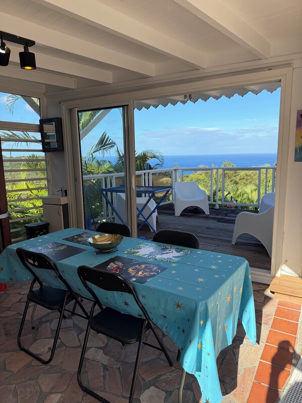 Ein überdachter Essbereich im Freien mit einem Tisch für zwei Personen, Stühlen und Blick auf das Meer.