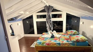 Een slaapkamer met een houten bed, een groot raam en een schuin dak.