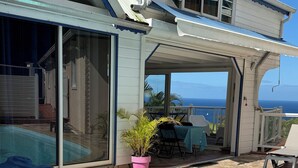 Een woonhuis met een zwembad, een overdekt terras met tuinmeubilair en uitzicht op zee.