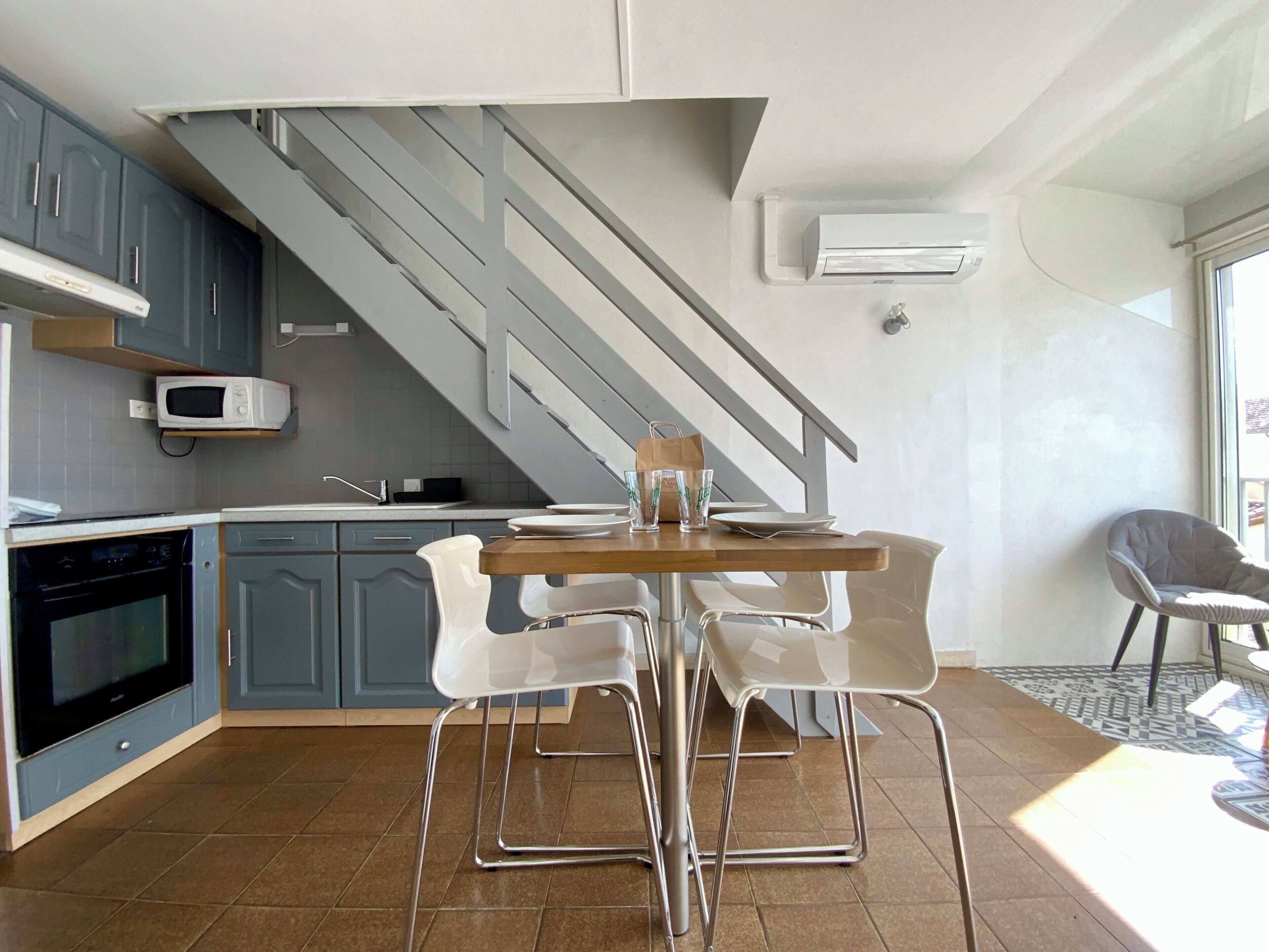 A modern kitchen with grey cabinets, a wooden dining table, and a staircase.