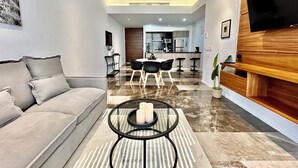 Un salon moderne avec un canapé, une table basse ornée de bougies et une cuisine en arrière-plan.