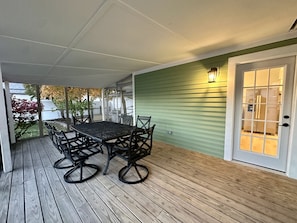A covered patio with a wooden deck, a table with chairs, and a green wall with a door.