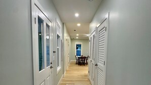 A hallway with white doors, a patterned rug, and a dining area in the background. - Cozy Cottage Retreat • 5 Min to Cedar Point • Deck + Screened Patio (Sandusky)