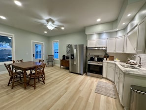 A modern kitchen with a dining area, wooden chairs, a refrigerator, stove, and a window with a view.