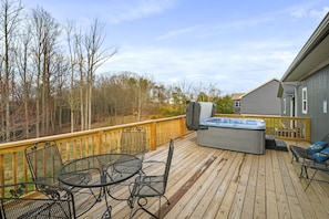 Une terrasse en bois avec des meubles d’extérieur, un jacuzzi et une vue sur les arbres et une maison.