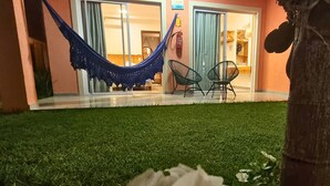 A hammock in front of a building with two chairs and a door. - Chalet with private garden, ideal for couples and families with children. (São Miguel do Gostoso)