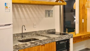 A modern kitchen with a double sink, wooden cabinets, a built-in oven, and a window overlooking a balcony. - Chalet with private garden, ideal for couples and families with children. (São Miguel do Gostoso)