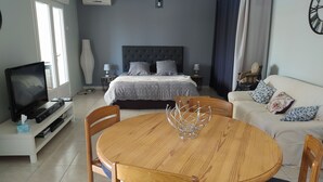 A bedroom with a bed, bedside tables, a TV, and a dining area with a table and chairs. - Quiet, independent studio between pine forest and sea. (Nissan-lez-Enserune)