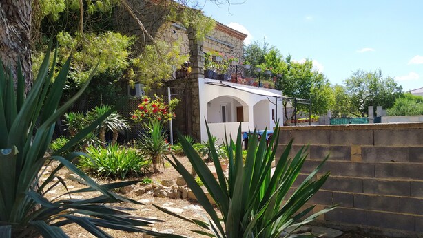 A garden with various plants and a white building with arched windows. - Quiet, independent studio between pine forest and sea. (Nissan-lez-Enserune)