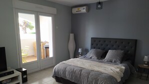 A bedroom with a large bed, a television, a coffee table, and a sliding door leading to an outdoor area. - Quiet, independent studio between pine forest and sea. (Nissan-lez-Enserune)