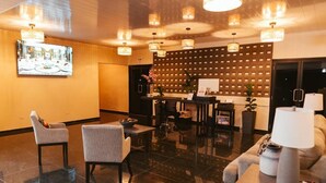 A lobby with a reception desk, two armchairs, a sofa, and a table with a lamp. - Hotel Plaza Los Tucanes (Nuevo Santiago)