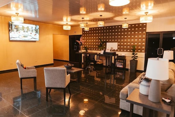 A lobby with a reception desk, two armchairs, a sofa, and a table with a lamp.