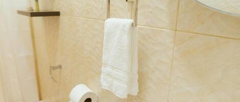 A bathroom with a toilet, a roll of toilet paper, and a towel hanging on a metal towel rack.