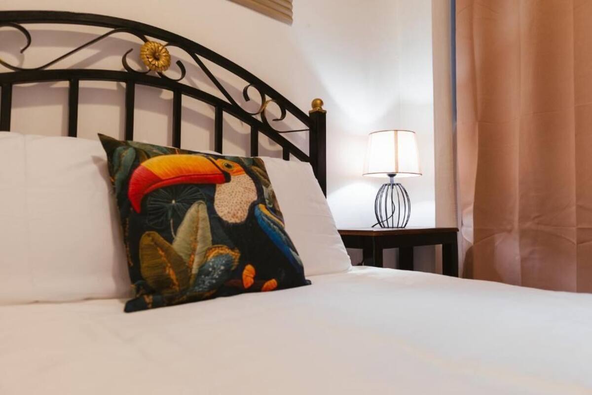 Un lit avec un oreiller coloré, une lampe de chevet et un rideau.