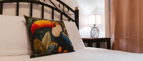 Una cama con un cojín colorido, una lámpara de noche y una cortina.