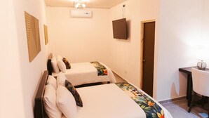A hotel room with two single beds, a desk with a chair, a television, and a door. - Hotel Plaza Los Tucanes (Nuevo Santiago)