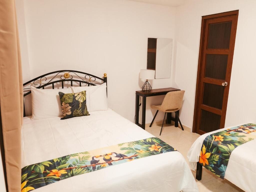 A hotel room with two beds, a desk, a chair, a mirror, and a door.