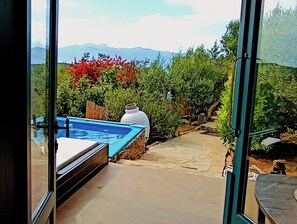 En vy genom en glasdörr ut mot en trädgård med en bubbelpool, ett trädäck och en stensatt gång som leder fram till en bergssluttning i bakgrunden.
