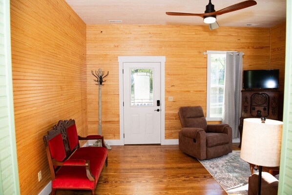 Una habitación con paredes de madera, un ventilador de techo, un sofá rojo, un sillón marrón, un televisor y una lámpara.