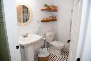 A bathroom with a white sink, toilet, and a mirror. There are wicker baskets on the floor and shelves above the toilet. - Laura & Almanzo`s home 1898-1910 (Mansfield)
