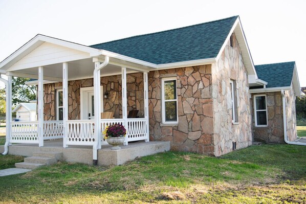 A two-story house with a stone facade, a covered porch with white railings, and a dark roof. - Laura & Almanzo`s home 1898-1910 (Mansfield)