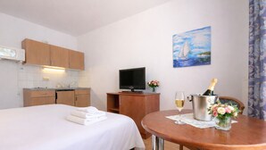 Ett hotellrum med en säng, ett litet pentry, en tv, en tavla, ett bord med en flaska champagne och ett glas vin.