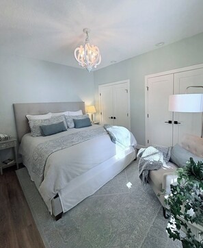 Ein Schlafzimmer mit einem großen Bett, Nachttischen, einem Chandelier, Einbauschränken und einer Nachttischlampe.