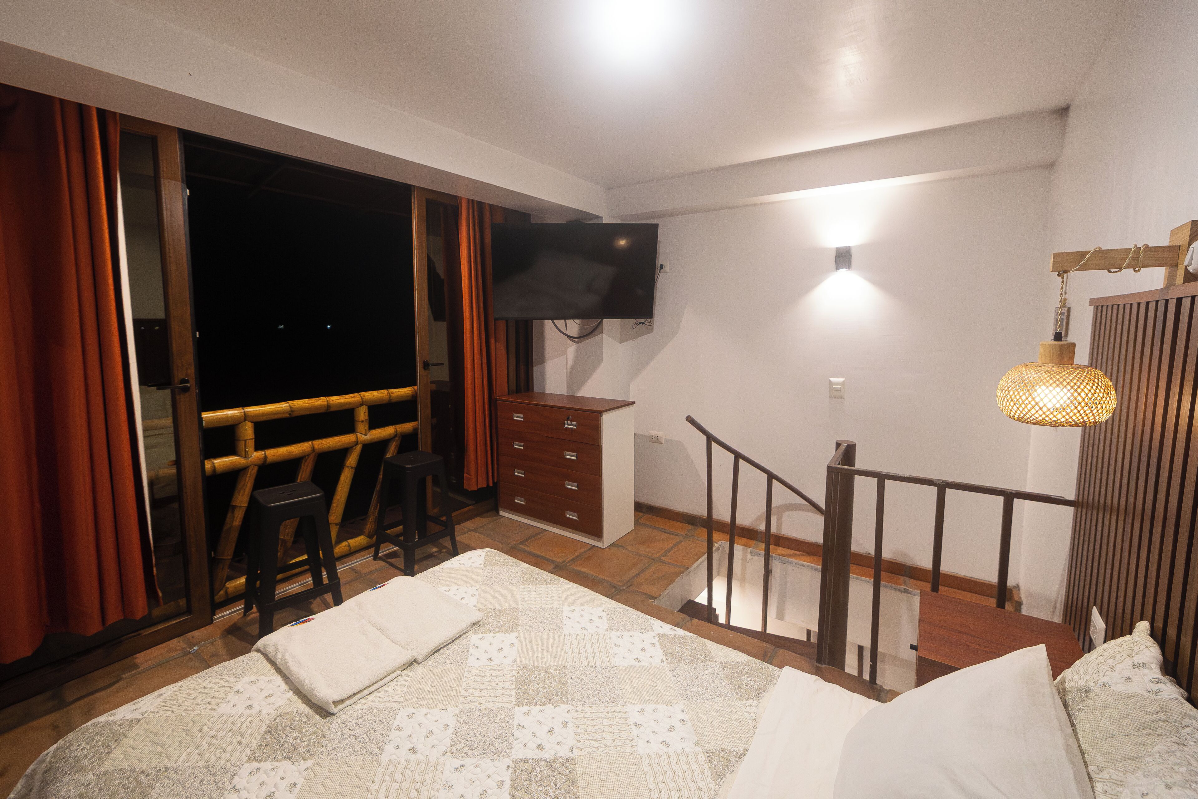 A bedroom with a bed, a TV, a dresser, a chair, and a staircase.