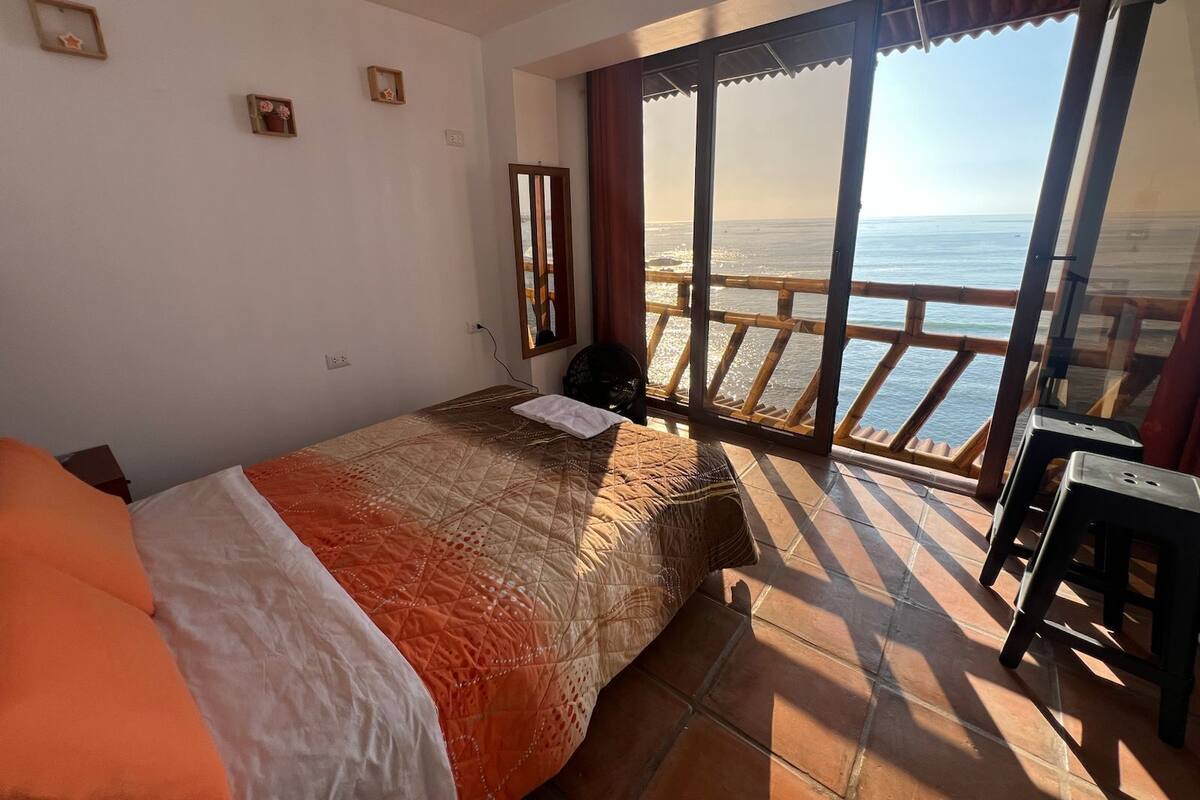 A bedroom with a bed, a desk, and a view of the sea through large windows.