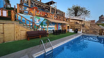 Un área de piscina con terraza de madera, un mural y zona de estar.