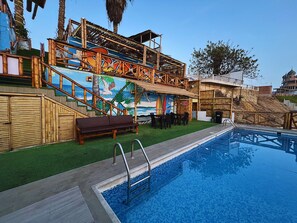 Un espace piscine doté d’une terrasse en bois, d’une fresque murale et d’un coin salon.
