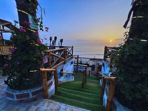 Un escalier menant à une plage offrant une vue sur le coucher de soleil, entouré de verdure et bordé de barrières en bambou.