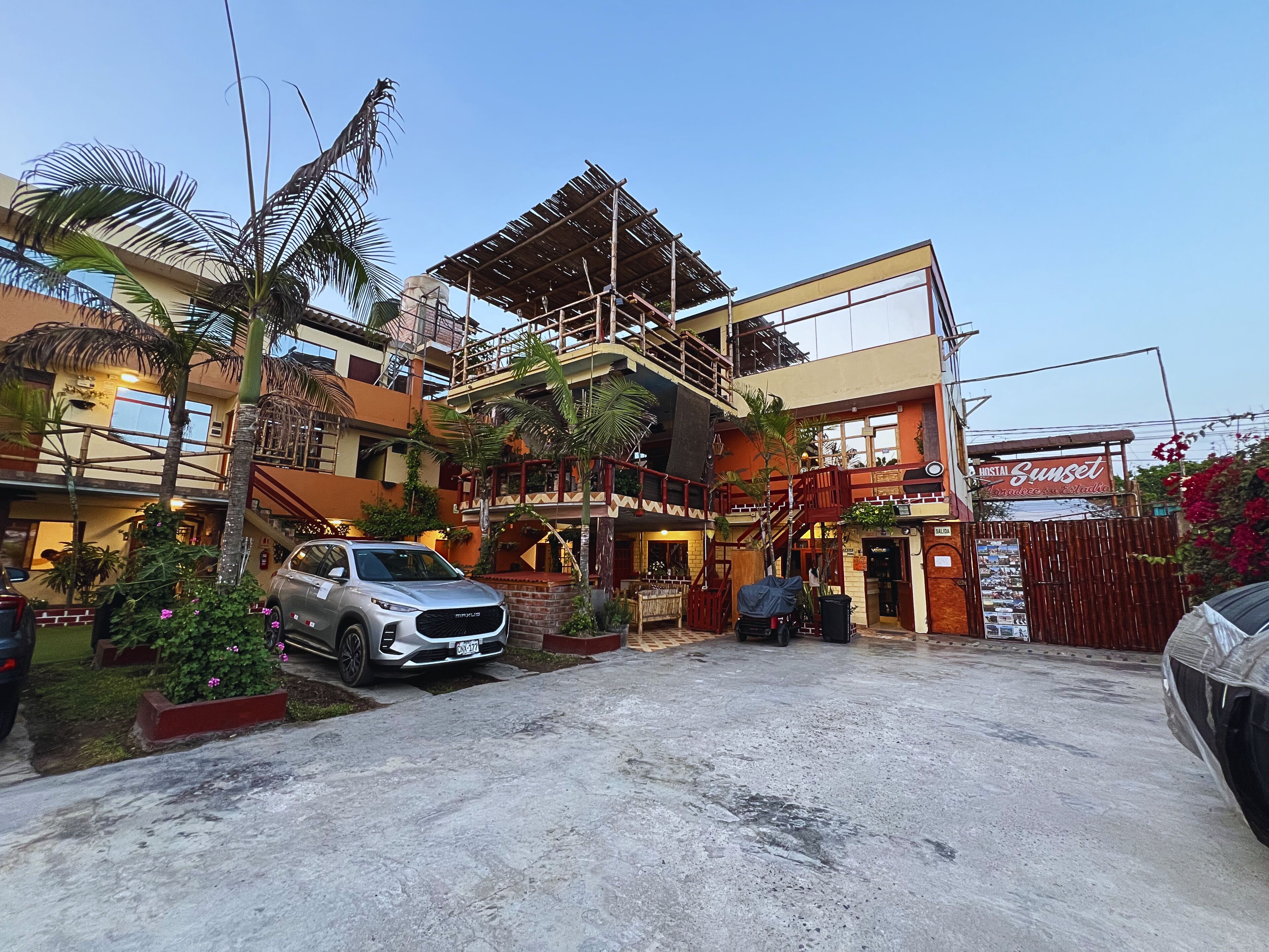 A multi-story building with a covered outdoor area, a car parked in front, and a sign for 'Sunset'.