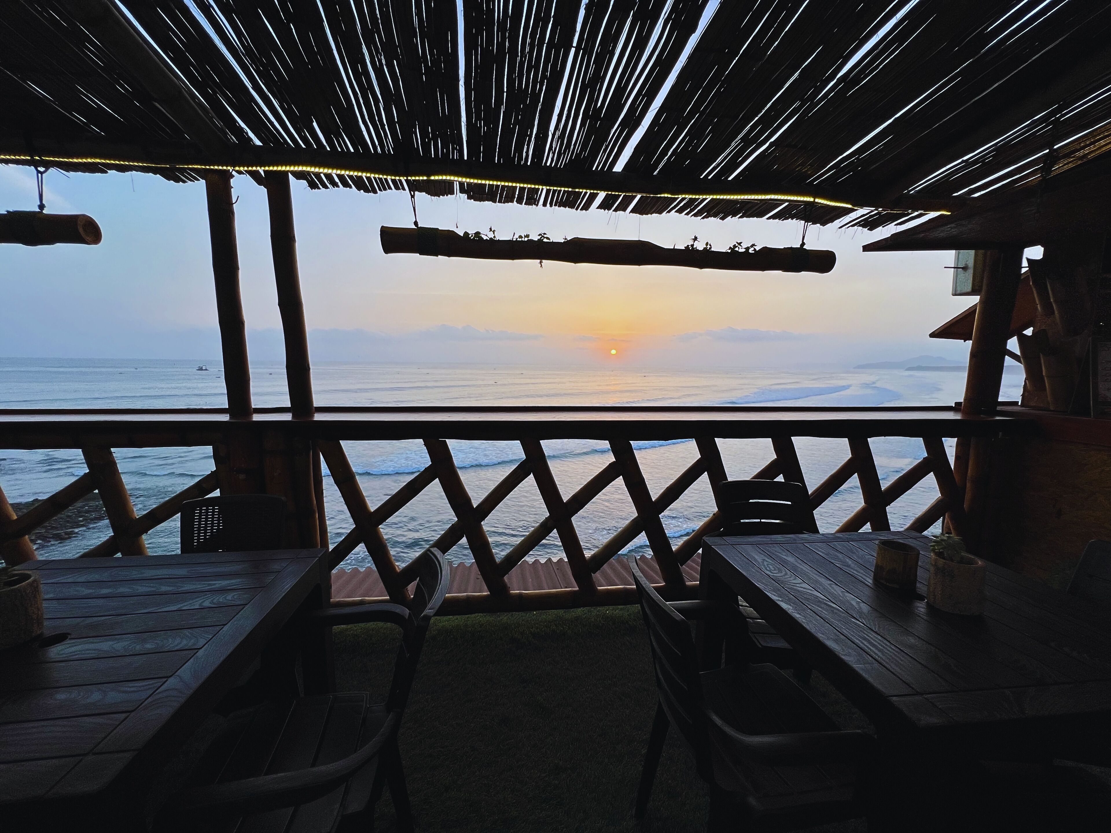 A wooden deck with a railing overlooking the ocean at sunset.