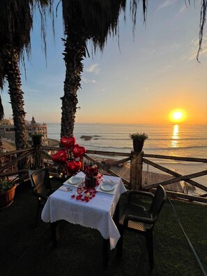 An outdoor dining table set with red heart-shaped decorations, overlooking a sunset over the sea. - Hotel Sunset Chancay (Chancay)