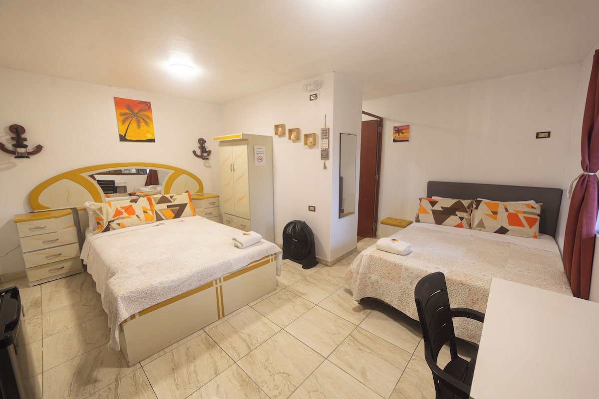 A hotel room with two beds, a desk, a chair, a mirror, and a door.