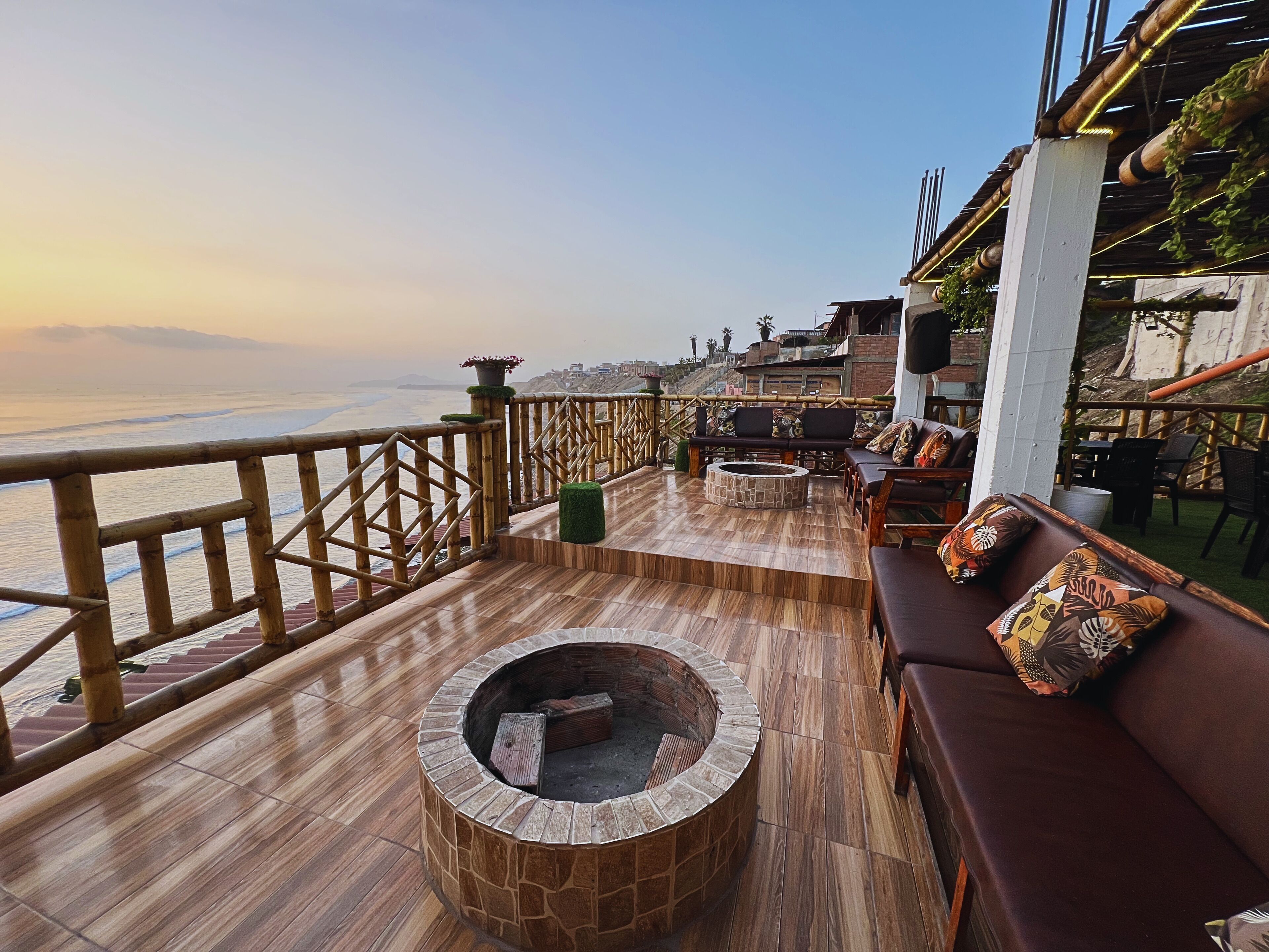 Eine Holzterrasse mit einem Steinkamin, Sitzgelegenheiten im Freien und Blick auf das Meer.