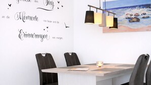 A dining area with a table, chairs, a candle, and a wall with a painting and text. - Welcome to “Strandmuschel” – the largest of our cozy one-room apartments. (Ostseebad Binz)