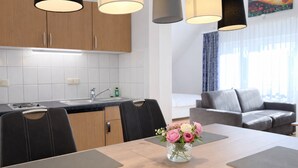 A modern kitchen with wooden cabinets, a built-in stove, and a dining area with a table and chairs. - Welcome to “Strandmuschel” – the largest of our cozy one-room apartments. (Ostseebad Binz)