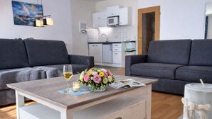 Een moderne woonkamer met twee grijze banken, een houten salontafel met een bloevas, een kaars en een glas wijn.