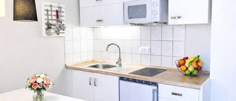 Eine moderne Küche mit weißen Schränken, einer Edelstahl-Spüle, einer Mikrowelle und einer Obstschale auf der Arbeitsfläche.