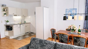 Una cucina moderna con mobili bianchi, un'area pranzo con tavolo e sedie in legno, e un soggiorno con divano.