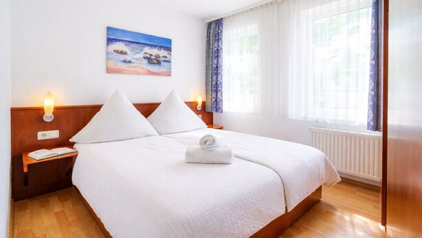 Un letto rifatto con lenzuola bianche, un quadro raffigurante una spiaggia e un comodino con una lampada e un libro.