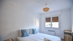 Ein Schlafzimmer mit einem Bett, Nachttischen, einem Fenster mit Jalousien und einer Deckenleuchte.