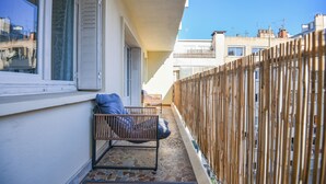 Ein Balkon mit Holzlattenzaun, gepolsterten Sitzgelegenheiten und Blick auf benachbarte Gebäude.