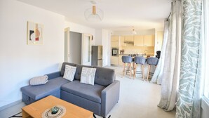 Ein modernes Wohnzimmer mit einem grauen Sofa, einem Holztisch und einer Küche im Hintergrund.